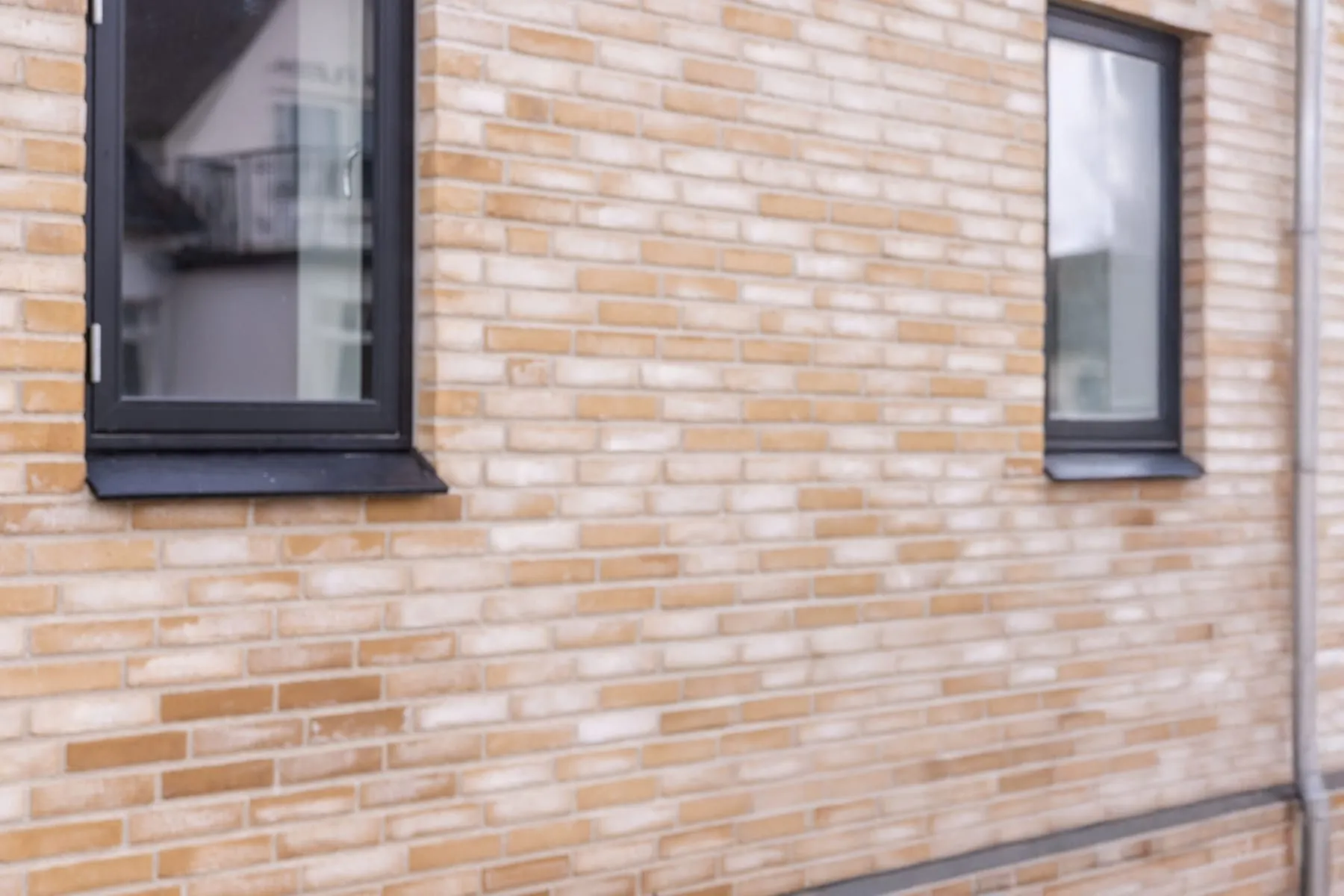 Detalje af murfacade med sort vindue og nedløbsrør